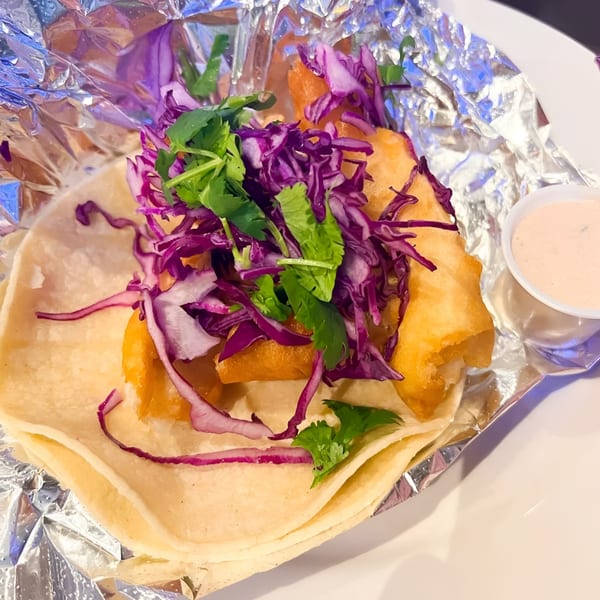 A Berryhill Baja Grill fish taco with fried fish, purple cabbage, and cilantro, served with sauce.