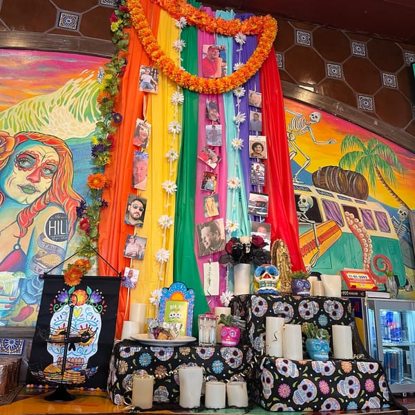 A vibrant Dia de los Muertos altar with colorful fabrics, photos, candles, and sugar skulls.