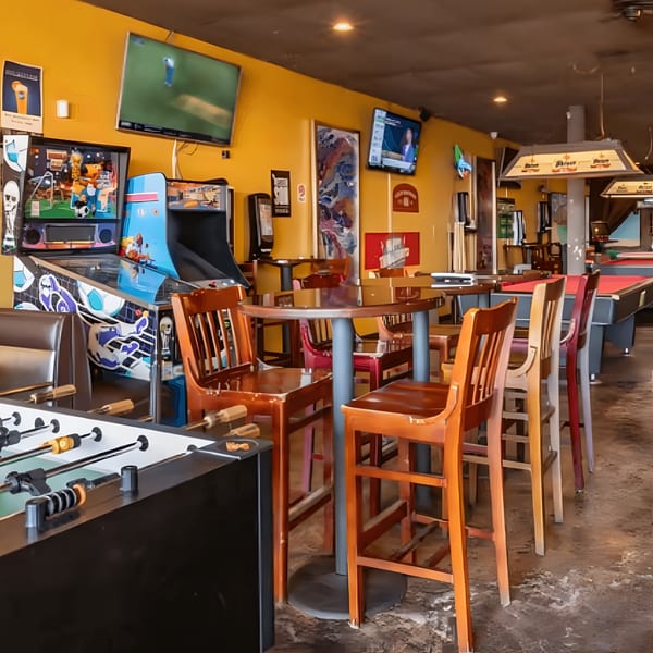A vibrant game room with arcade machines, a foosball table, high-top tables, and a pool table.