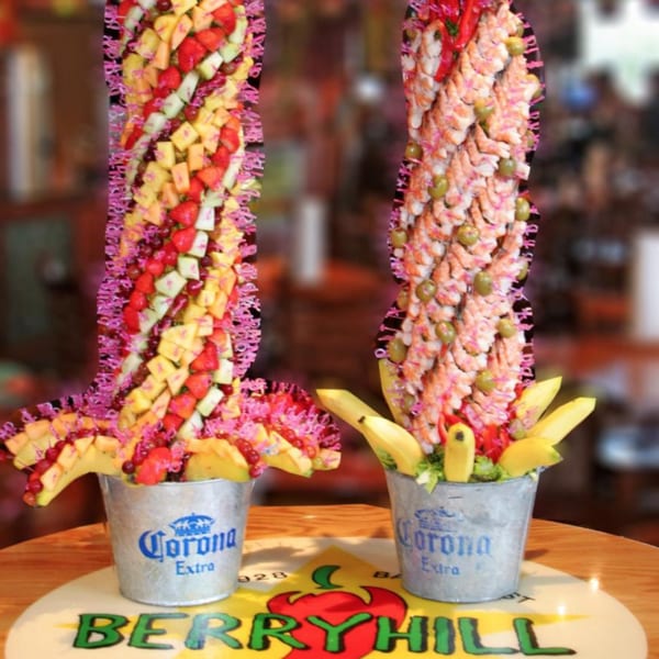 Two tall, colorful fruit and shrimp towers in Corona buckets on a Berryhill Baja Grill table.